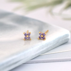Macro detail of gold four-leaf clover stud earrings with purple cubic zirconia stones