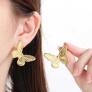 Detail of golden butterfly stud earrings with vintage texture on a model and hand