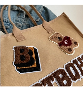 Detail of plush bear embroidery and B logo patch on khaki canvas tote bag