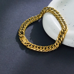 Dettaglio del bracciale a catena cubana dorata su ceramica bianca e sfondo grigio scuro