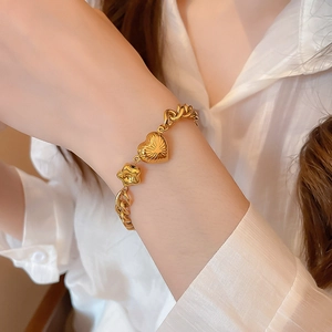 Detailed close-up of a golden charm bracelet featuring a heart and flower on a woman's wrist