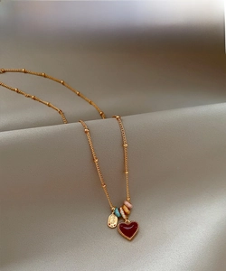 Close-up of 18k gold-plated bead chain with red enamel heart pendant on grey silk fabric
