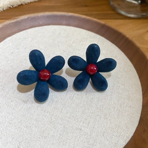 Detailed close-up of navy blue flocked flower earrings with a red center on a beige cushion