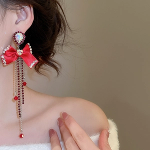Close-up of red bow tassel earrings with sparkling rhinestones worn by a model