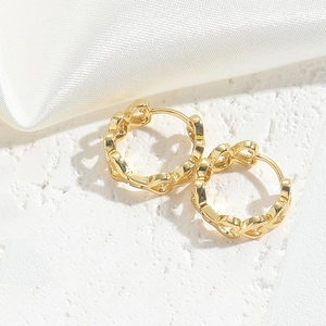 Close-up of golden heart-shaped chain hoop earrings on a white stone surface