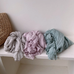 Folded pleated silk scarves in gray, light purple, and sage green on a white shelf