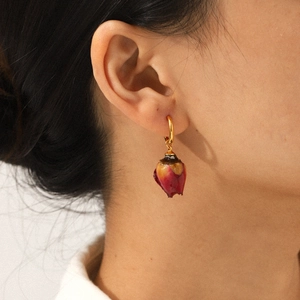 Elegant gold hoop earrings with dried red rosebud pendant worn by a model in close-up