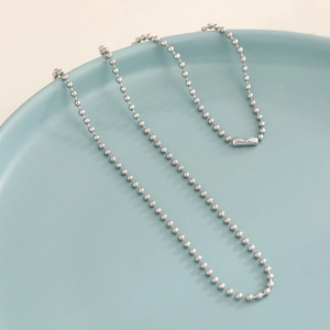 Polished silver bead chain necklace with rectangular connector on a blue ceramic plate