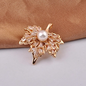 Detailed close-up of golden maple leaf brooch with zircon pavé and a white pearl on silk