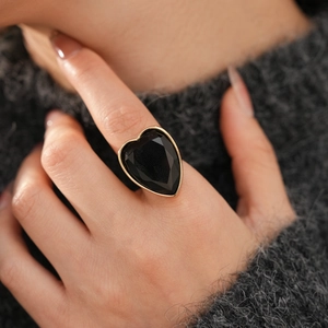 Close-up of heart-shaped ring with black zircon stone on gold band and knit background