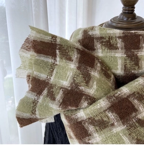 Close-up of the thick houndstooth knit texture and frayed fringe edges of the warm scarf