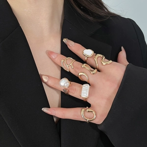 Detail of model wearing a stack of golden metal rings with pearls against black suit