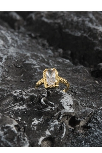 Detail shot of a gold ring with a rectangular crystal on a textured rock background