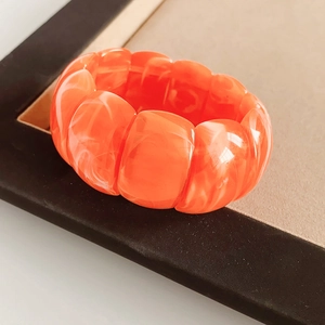 Macro detail of wide orange acrylic stretch bracelet with marble texture on display stand