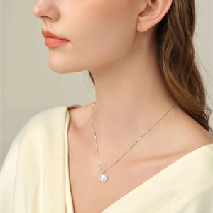 Close-up of a high-luster round white pearl pendant on a silver necklace worn by a model