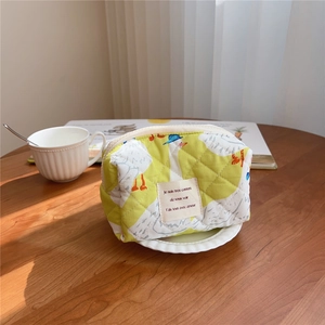 Detailed view of lime green quilted cotton makeup bag with goose print on wooden desk