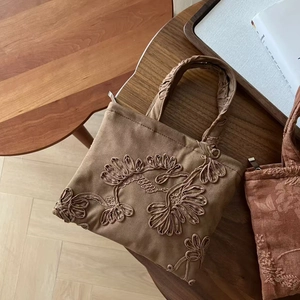 Close-up of vintage brown suede handbag with detailed floral embroidery and ruched handles