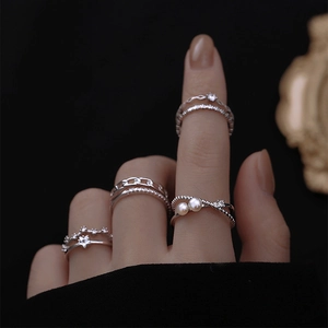 Detail of silver rings set with pearls and star motifs worn on fingers over black background