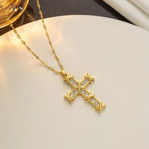 Close-up of a gold cross pendant necklace with zircon stones on a white textured plate