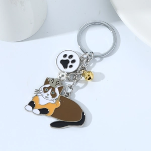 Detail of metal cat keychain featuring a golden crown, paw charm, and small bell
