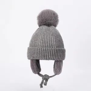 Detailed view of grey knit hat with faux fur pompom and braided chin straps