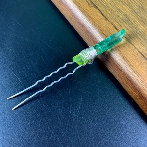 Detailed macro view of a green crystal hair fork with silver wire wrapping and dual wavy pins