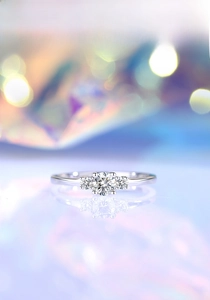 Detailed close-up of a three-stone moissanite ring with polished silver mirror reflection