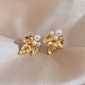 Détail de boucles d'oreilles feuille dorées avec perle blanche et cristal sur tissu soie