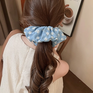 Detail of light blue floral scrunchie worn on a ponytail in a warm indoor setting