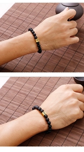 Detail of beaded bracelet featuring golden letter cubes F and H on black lava stones