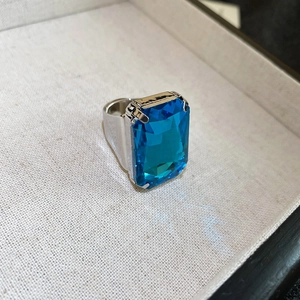 Macro view of blue rectangular crystal ring with silver four-prong setting on fabric tray
