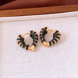 Detail of 18k gold heart-shaped earrings with black woven rope design on beige fabric