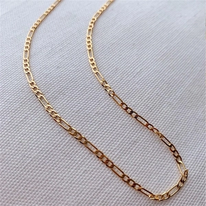 Close-up of golden Figaro chain necklace featuring a classic three-short-one-long link design