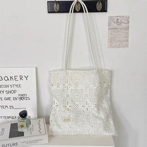 Detail of white lace tote bag with hollow floral crochet patterns and slim shoulder straps