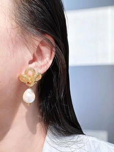 Detailed close-up of a vintage golden twist knot earring with a Baroque pearl on a model