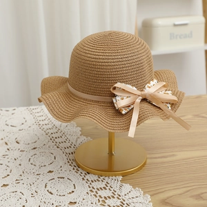 Détail d'un chapeau de paille tissé avec nœud floral et bord ondulé sur un support