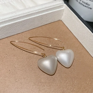 Macro view of gold-tone long hook earrings with shimmering white pearl heart pendants