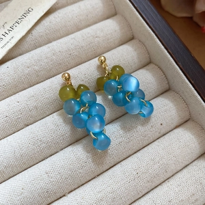 Detailed macro view of light blue resin grape earrings in a velvet jewelry box