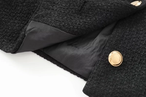 Detailed close-up of black tweed jacket texture with gold metal buttons and satin lining