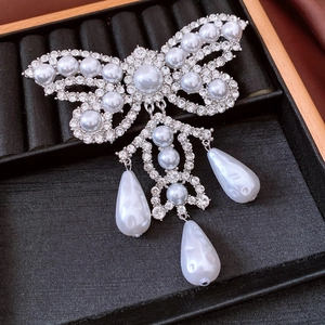 Macro detail of silver bow brooch with pavé rhinestones and hanging teardrop pearls