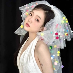 Detailed close-up of white mesh veil decorated with vibrant colorful pom-poms on model