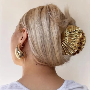 Detail view of golden shell hair claw and teardrop earrings worn by a model