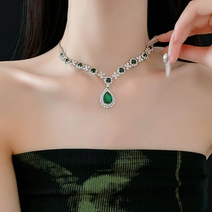 Detail of silver necklace with teardrop emerald pendant and small clear diamonds on model
