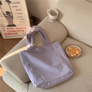 Detalle del bolso tote de lona lavanda con parche de letras y forro de cuadros en el asa