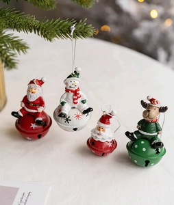 Detail view of four festive Christmas resin ornaments with iron bells on white surface