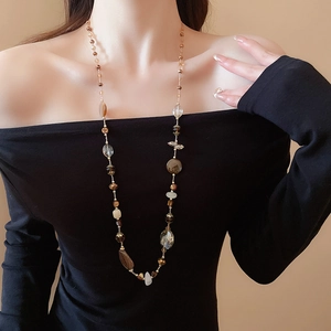 Dettaglio della collana lunga con perle color ambra e crema su abito nero elegante