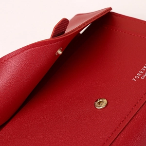 Macro detail of red leather phone bag with gold metal snap button and fine stitching