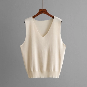 Detail of a beige knit V-neck vest hanging on a dark wood hanger with high-quality texture