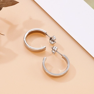 Detail view of silver C-shaped stainless steel earrings with butterfly back on warm beige