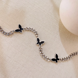 Macro detail of silver stainless steel chain bracelet with three black butterfly charms